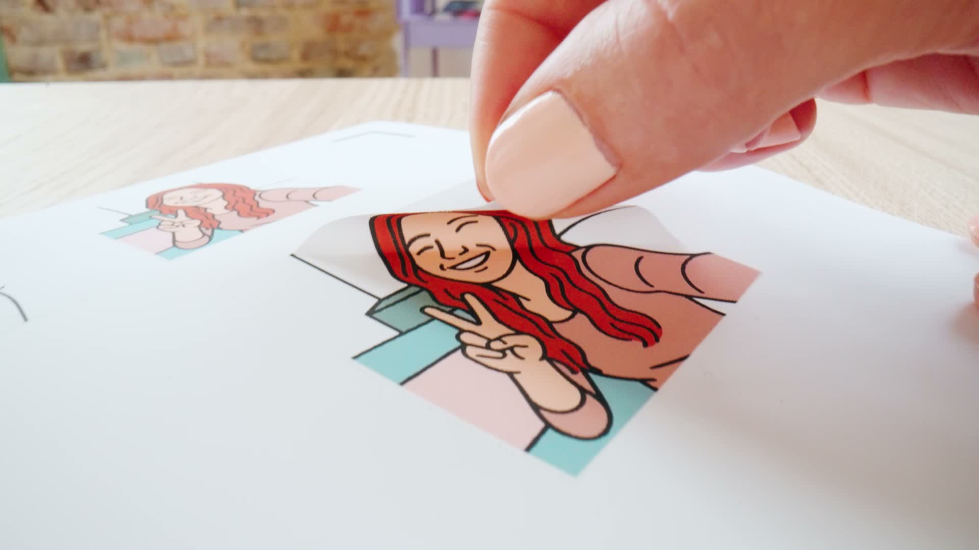 Close-up of a hand lifting a colourful illustrated sticker from a printed sheet.