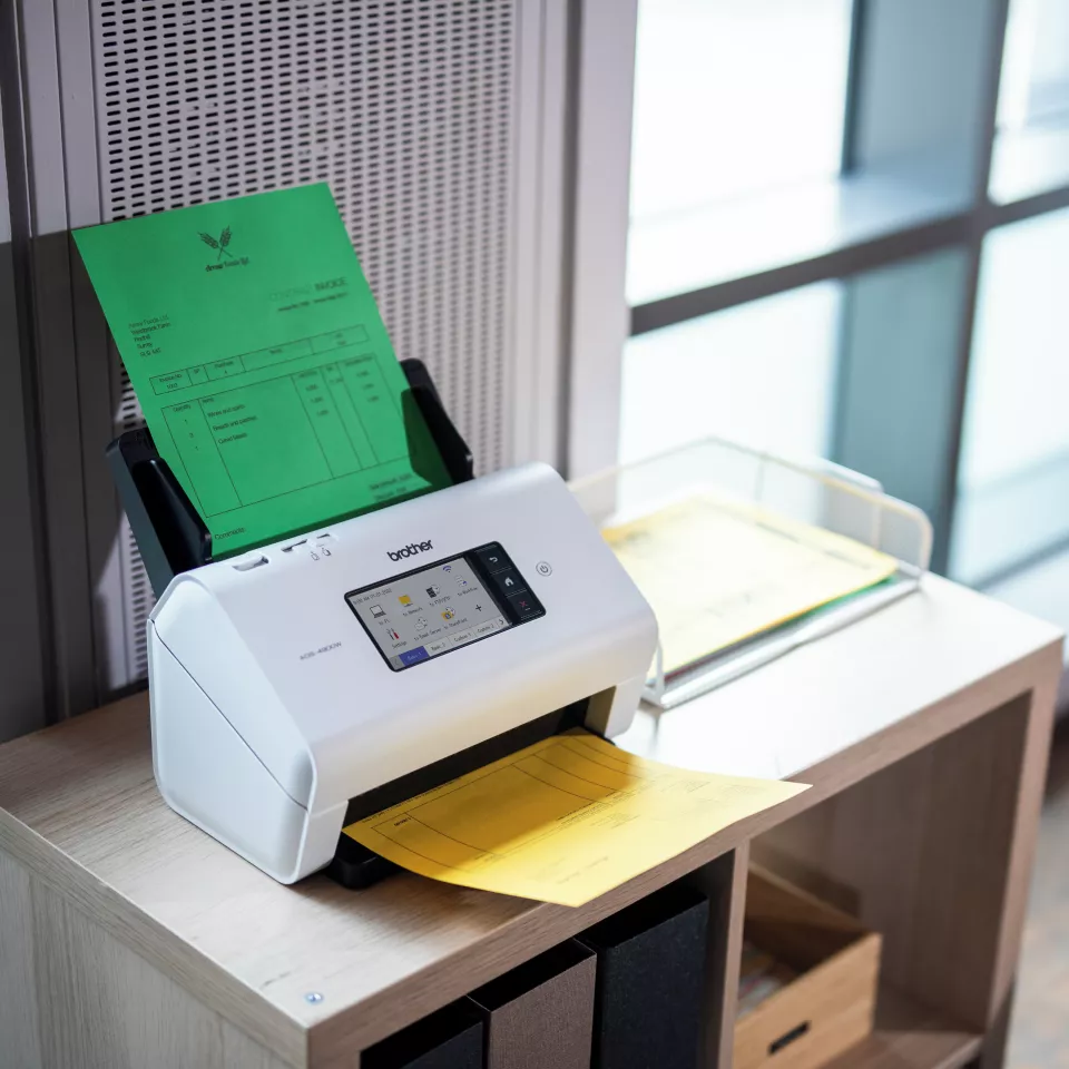 ADS-4900W sitting on a desk with paper in the feeder and lower tray
