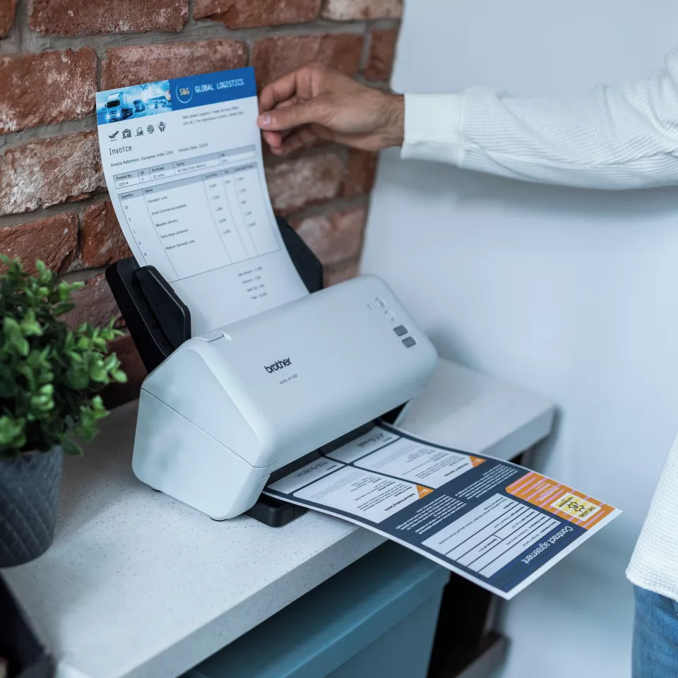 ADS-3100 sitting on a desk with a person inserting paper into the feeder