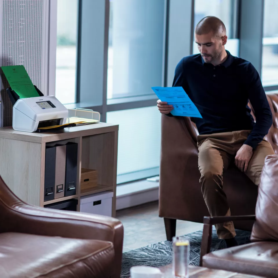 ADS-4900W on a desk with a person sitting next to it reading a sheet of paper
