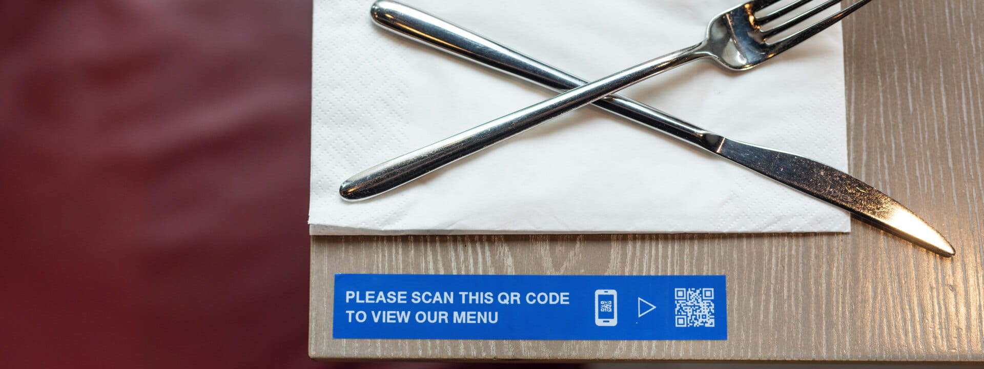 A knife and fork on a serviette with a QR code menu on a label in a restaurant.