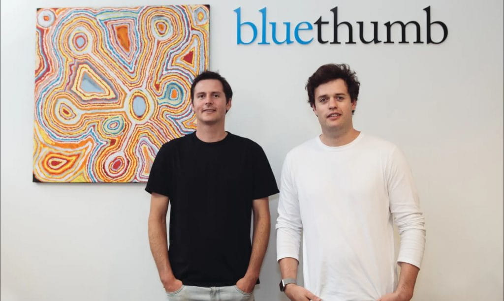 The Hartley brothers standing in front of indigenous art and Bluethumb logo