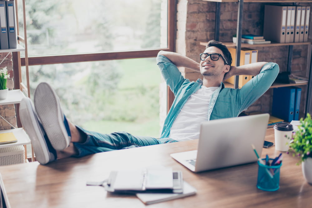 A young man relaxing at his desk in his home office with his feet up.