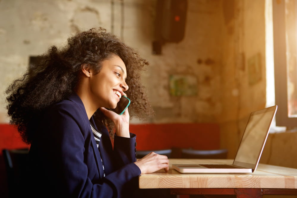 A young female office worker talking on the phone in front of a laptop.