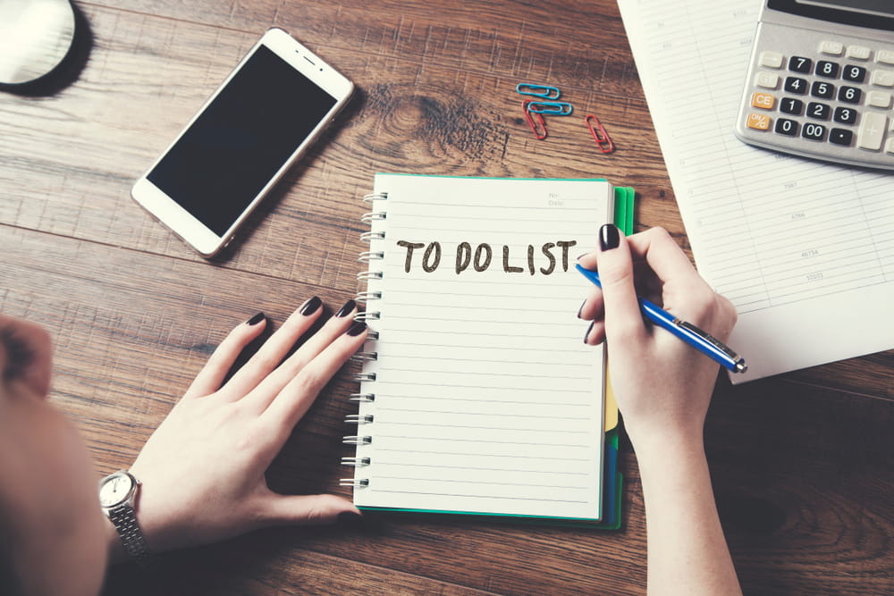 A lady writing down her to-do list on a WFH desk setup.