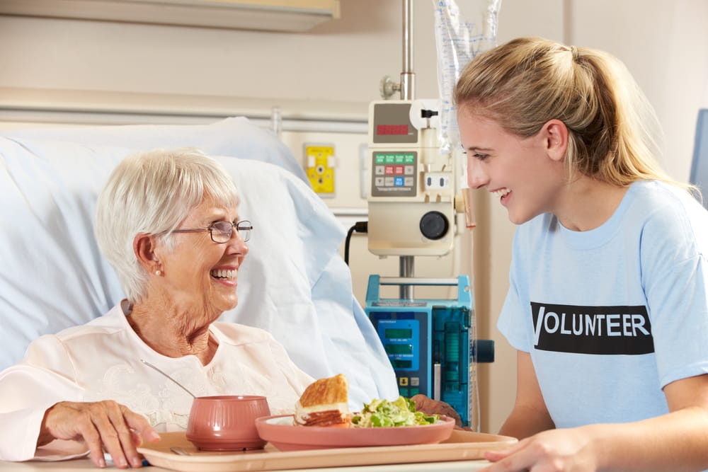 An elderly patient having her meal delivered by a young volunteer in a hospital.