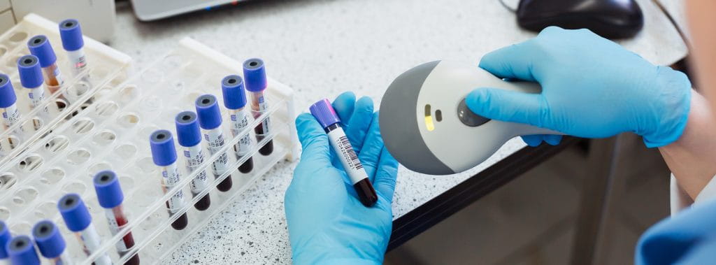 A lab worker scans a specimen label with blue gloves on.