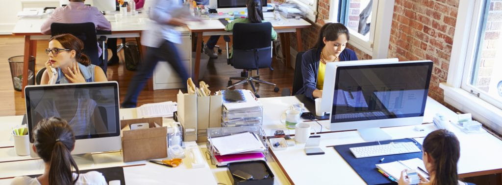 An open office plan with workers in front of computer screens while practicing social distancing measures.