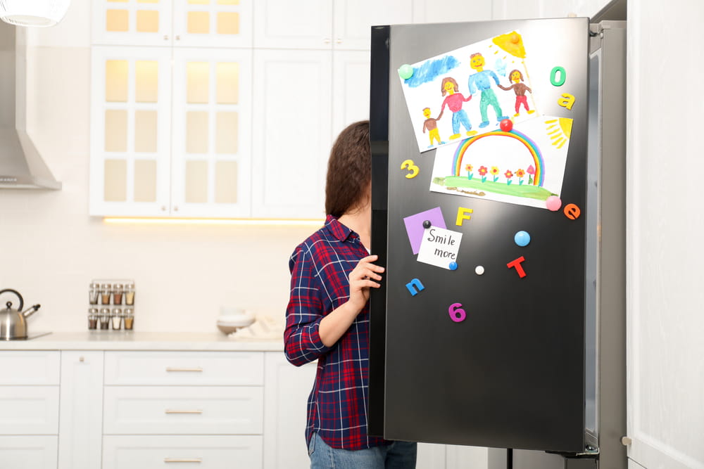 A lady opening and looking into a fridge with family drawings on it.