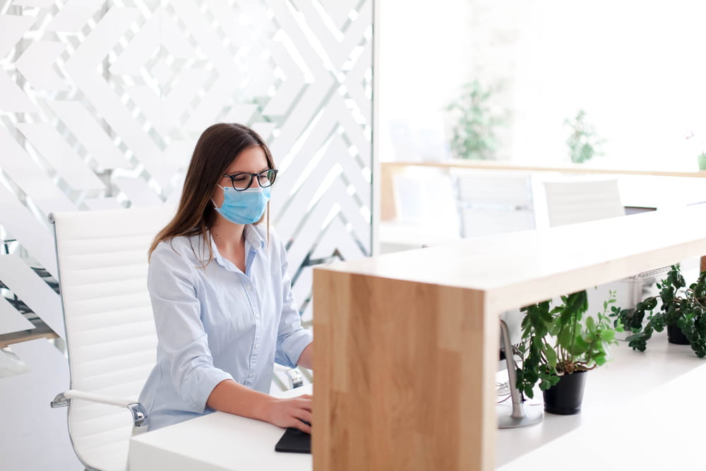 A lady at a front desk with a mask on checking visitors in.