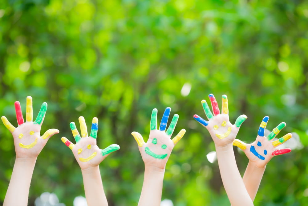 Childrens' hands with paint on them in the air in a backyard.