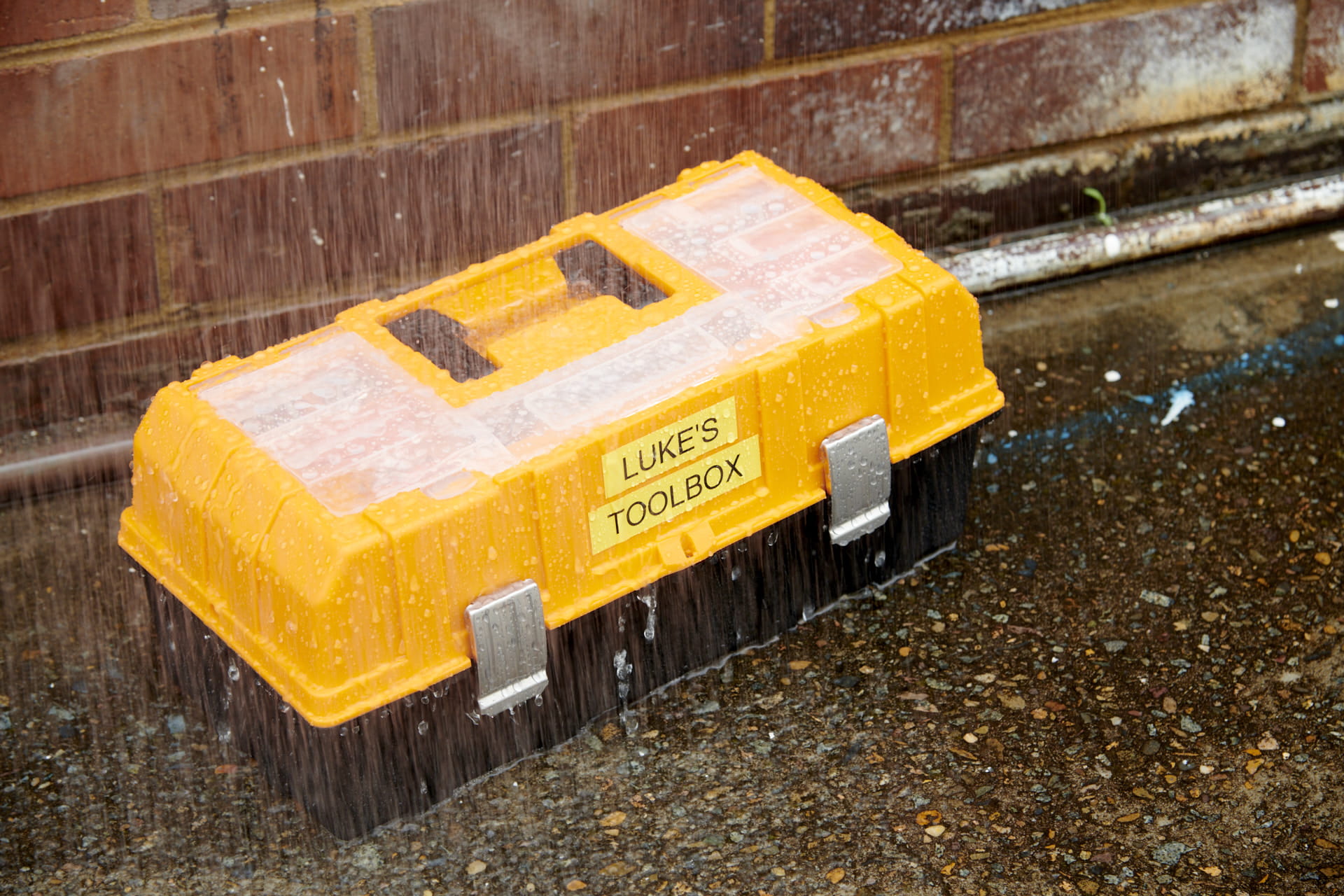 A yellow toolbox with a fade-resistant label on it outside in the rain.
