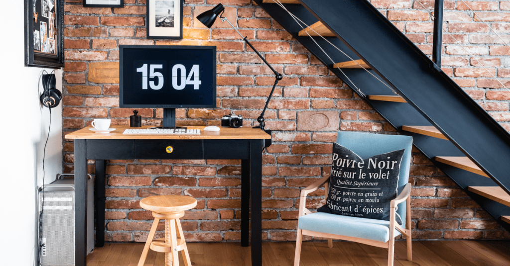 An industrial home office space with red bricks underneath a staircase.