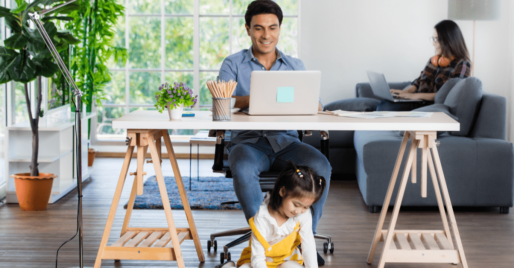 A husband and wife on their laptops with their daughter playing.