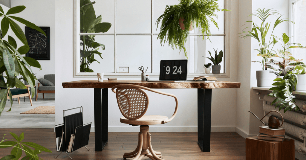 A neutral modern home office with lots of green plants and a wooden desk.