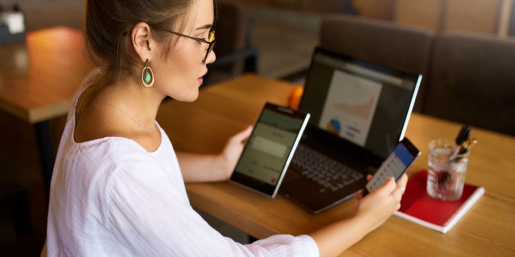 Young lady small business owner sitting down on phone, tablet and laptop