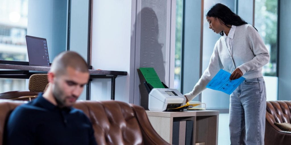 Man sitting down on lounge with woman in background scanning documents in a home office