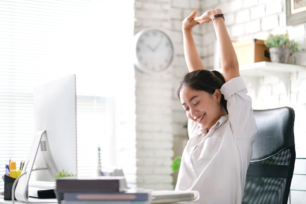 Young lady stretching in her home office workstation displaying good desk ergonomics