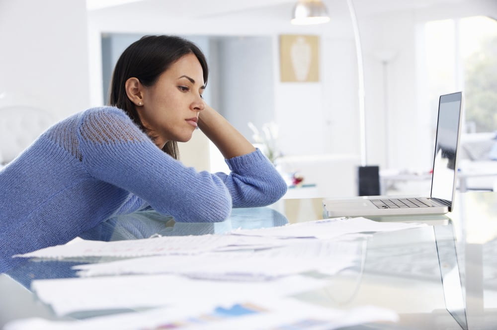 Lady leaning over desk in front on laptop at home office being unproductive.