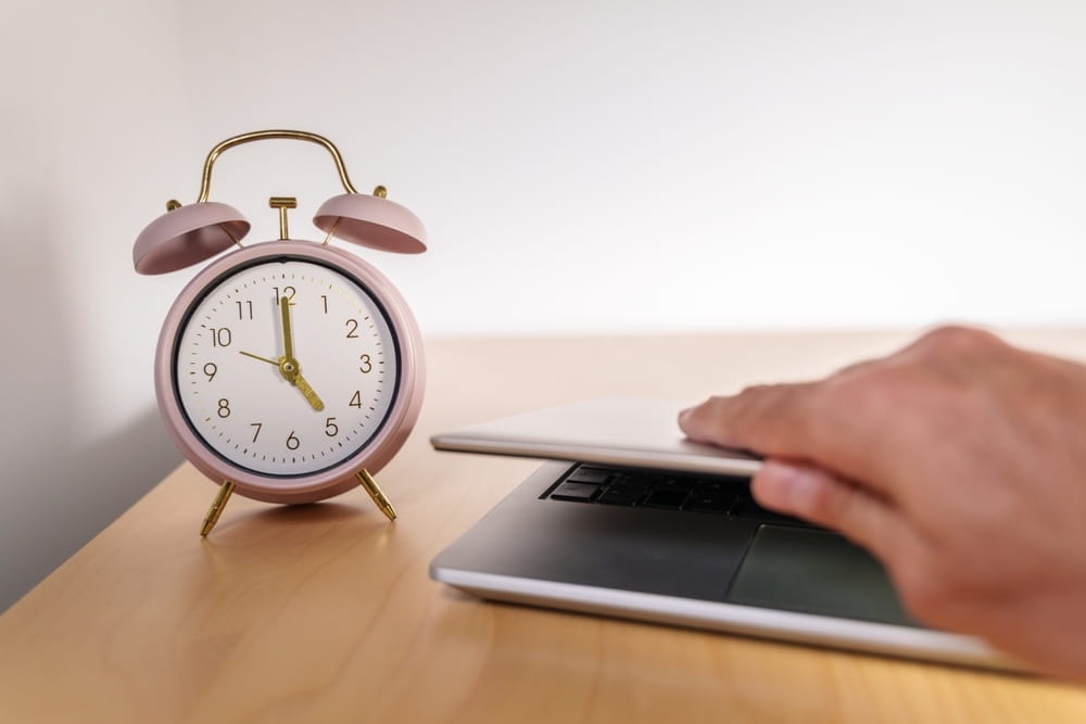 A clock next to a person shutting a laptop depicting exhaustion at work.