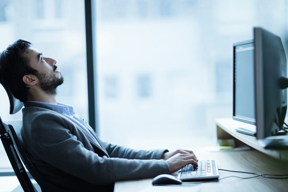 A man at his desk in the office looking up at the ceiling displaying signs of job burnout.