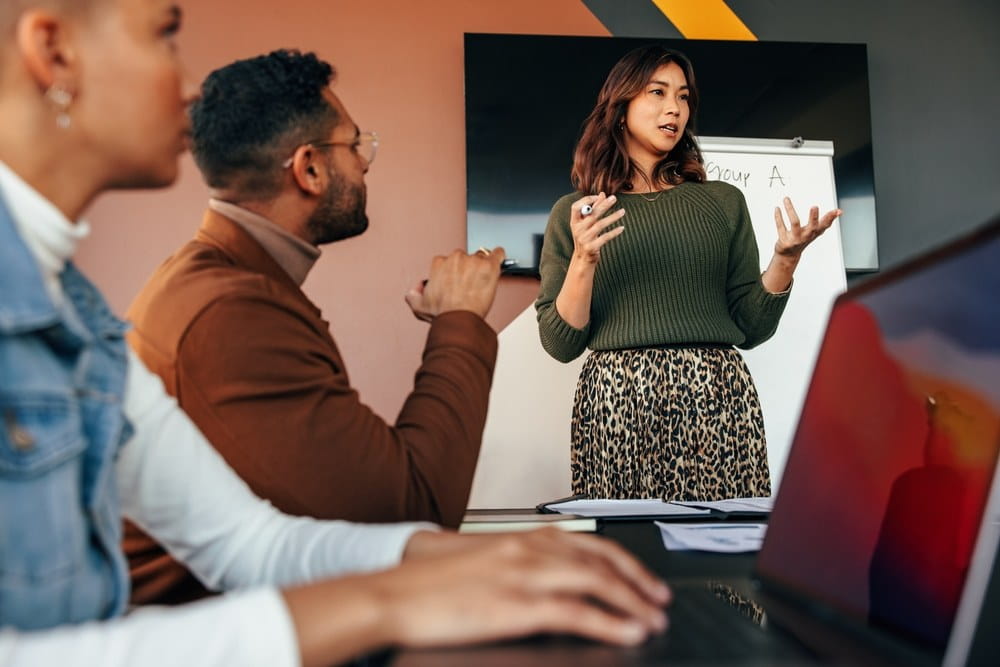 A businesswoman presenting to a boardroom of people in the office.