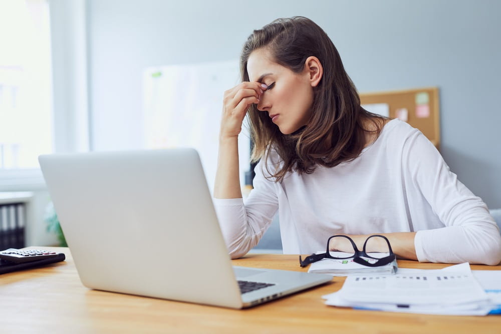 Lady stressed working from home in front of laptop on a desk filled with papers.