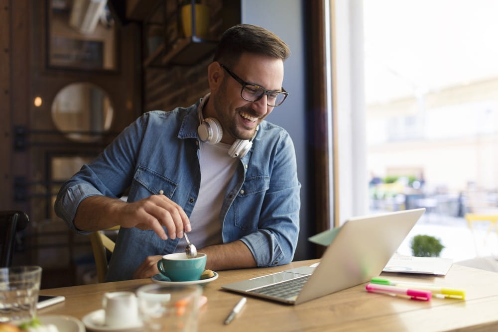 Young male working remotely in a cafe in front of a laptop while enjoying a coffee,