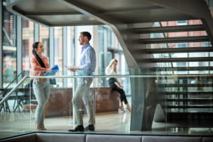 two workers talking in an office next to some stairs