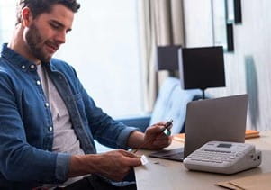 Man sitting at a desk with his laptop and a PT-D410 label printer