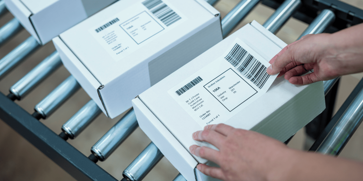 A person attaching shipping labels to parcels on a conveyor belt. 