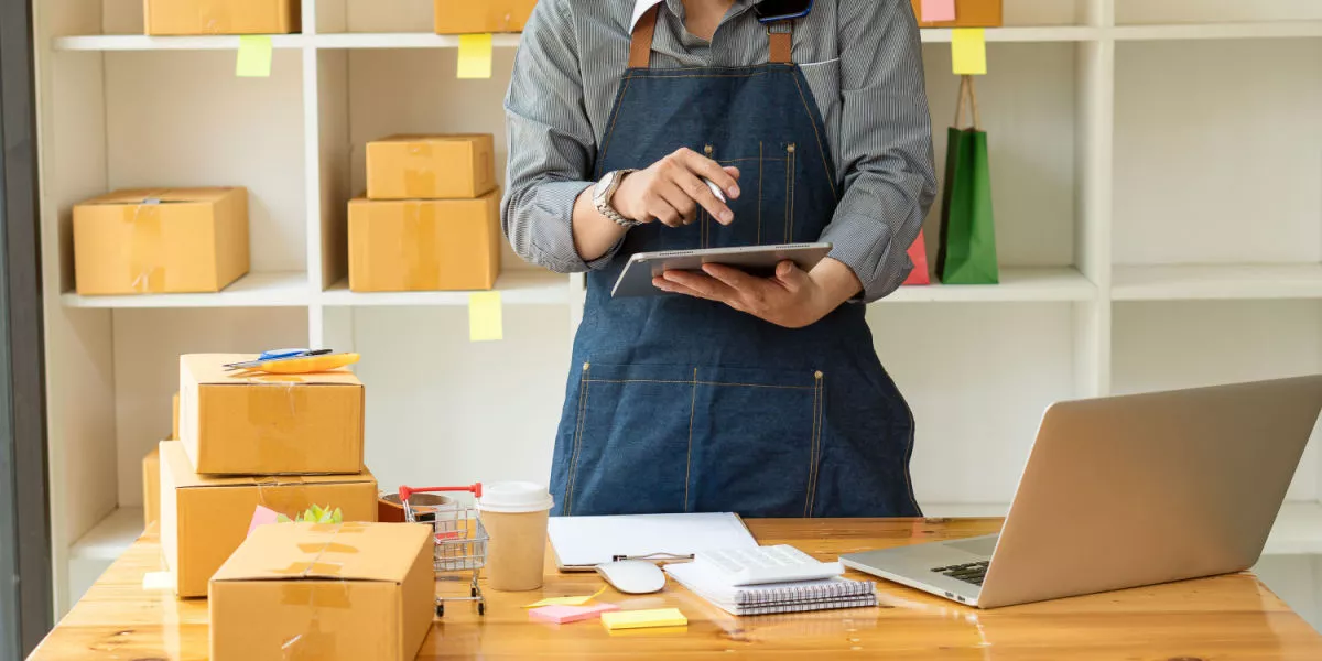 An online business owner using a tablet with packages on the desk