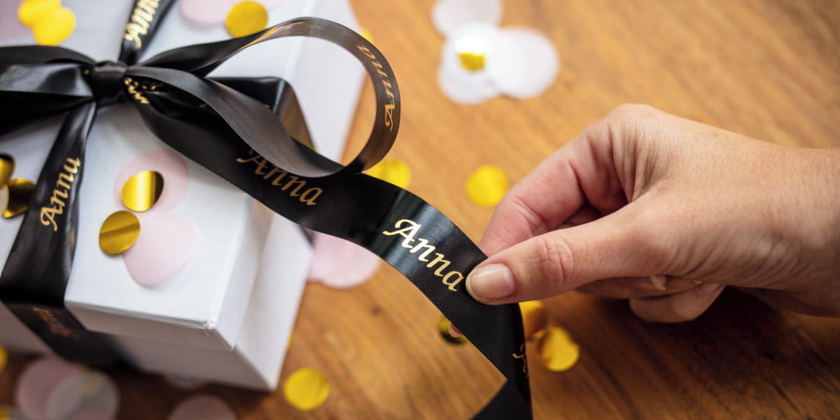 A hand touching a Brother TZe ribbon tape that's wrapped around a gift