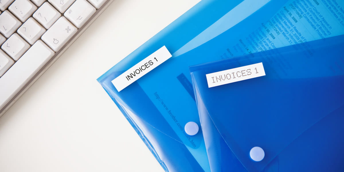 Brother TZe labels on blue folders in a home office setting next to a keyboard