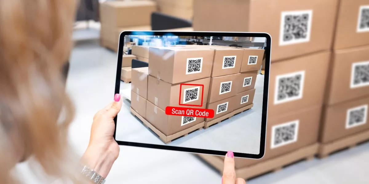 A woman in a warehouse scanning QR codes on stock with a tablet
