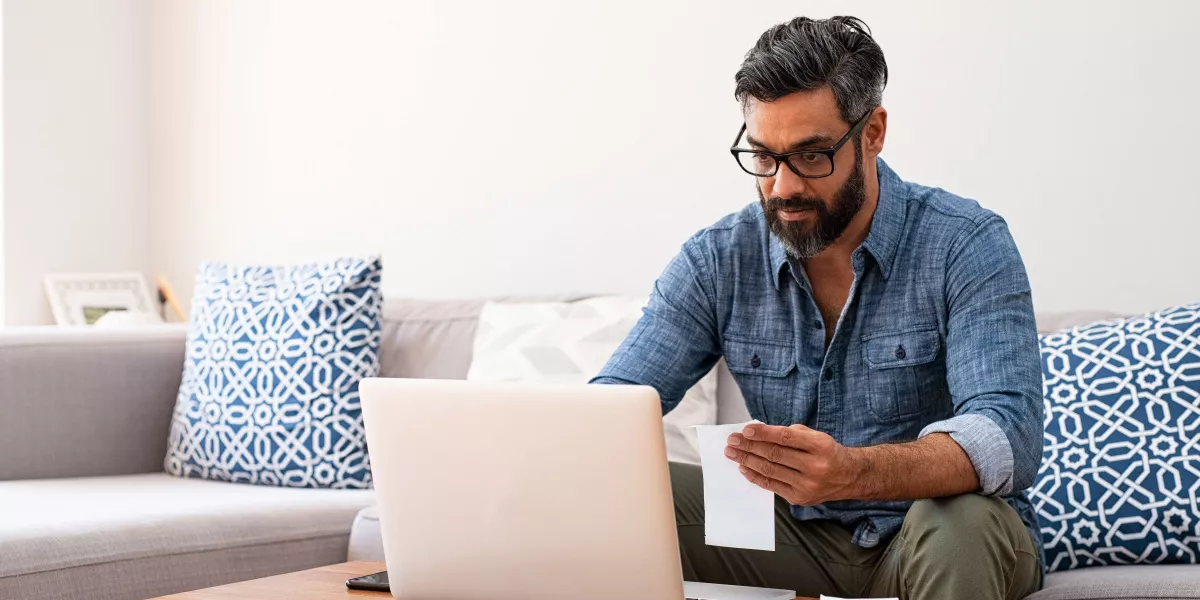 A man with an invoice in hand next to his laptop