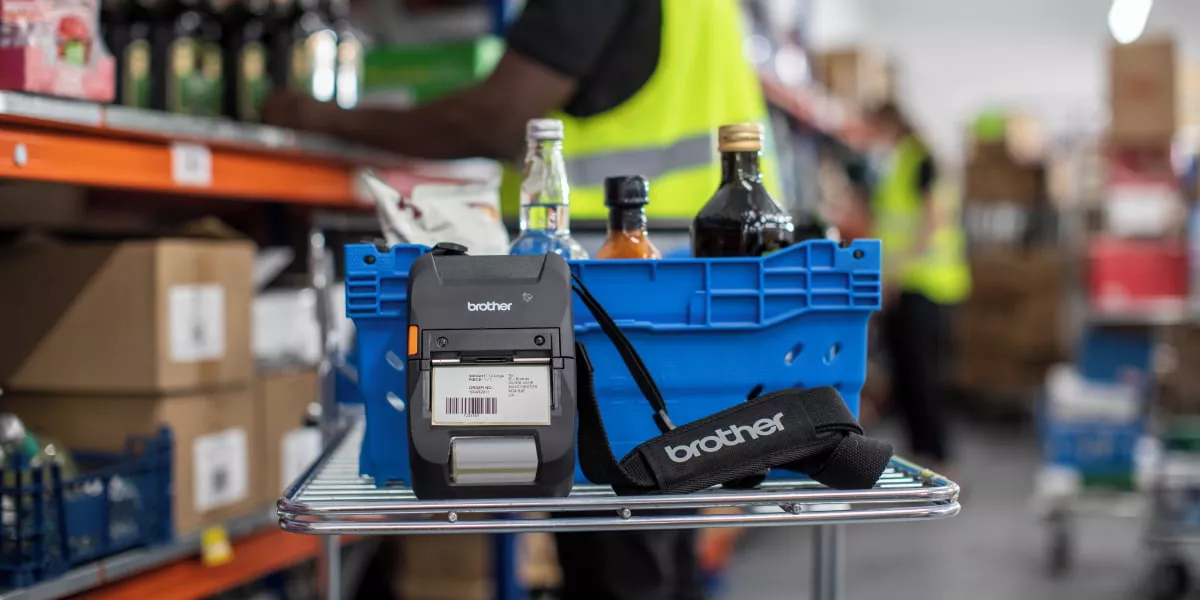 A Brother portable label printer in a warehouse next to stock