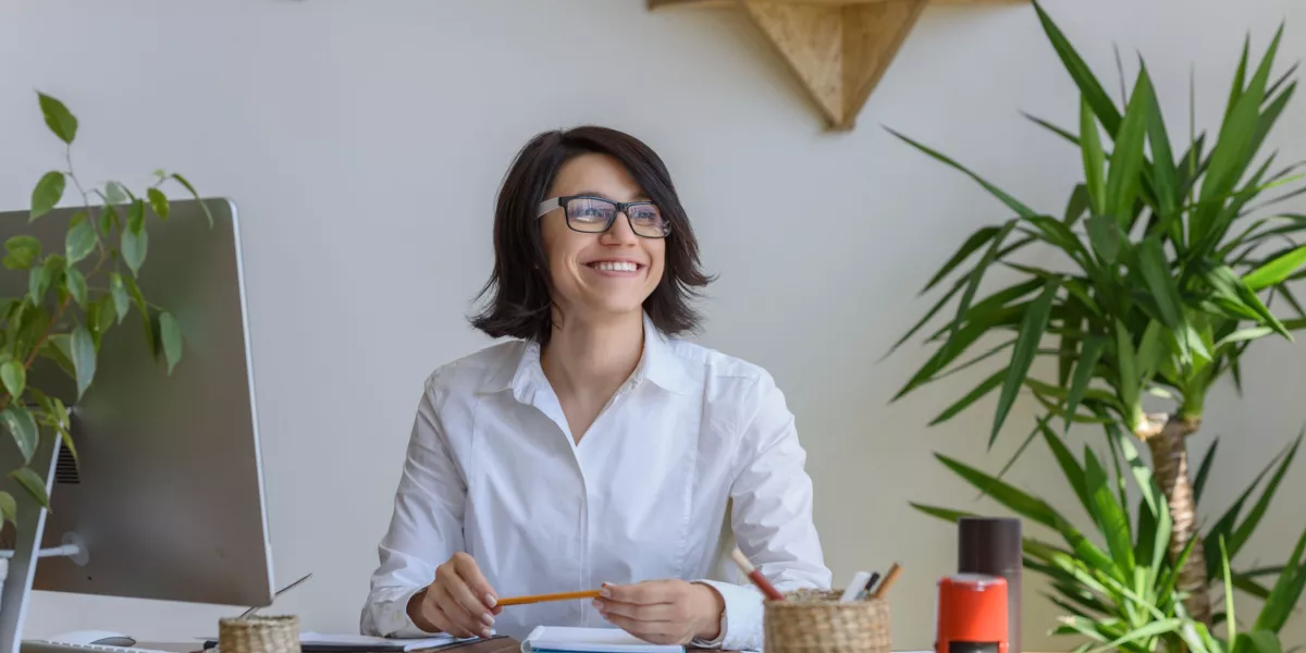 A lady smiling sitting down in a home office with plants around her
