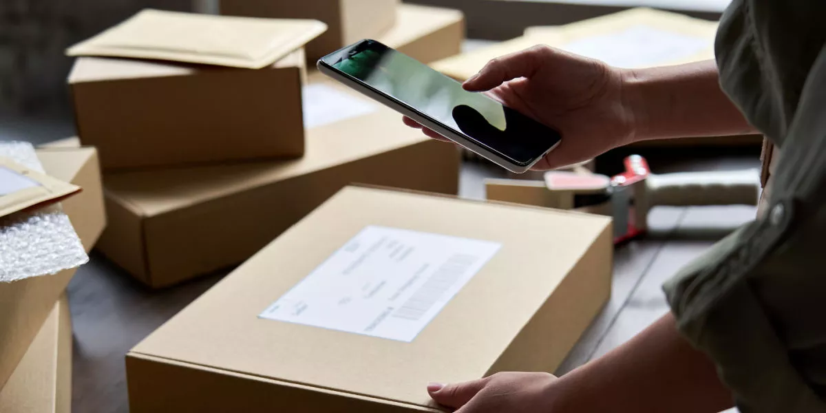 A business owner holding a parcel and smartphone scanning a shipping label
