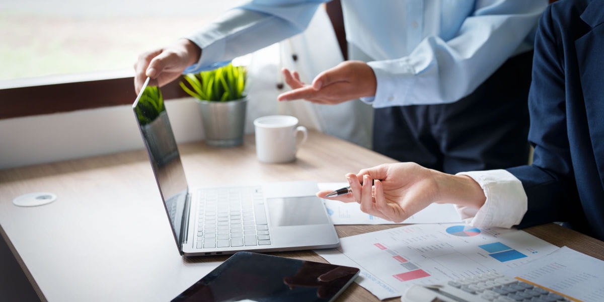 Office workers pointing to a laptop with graphs on the desk.