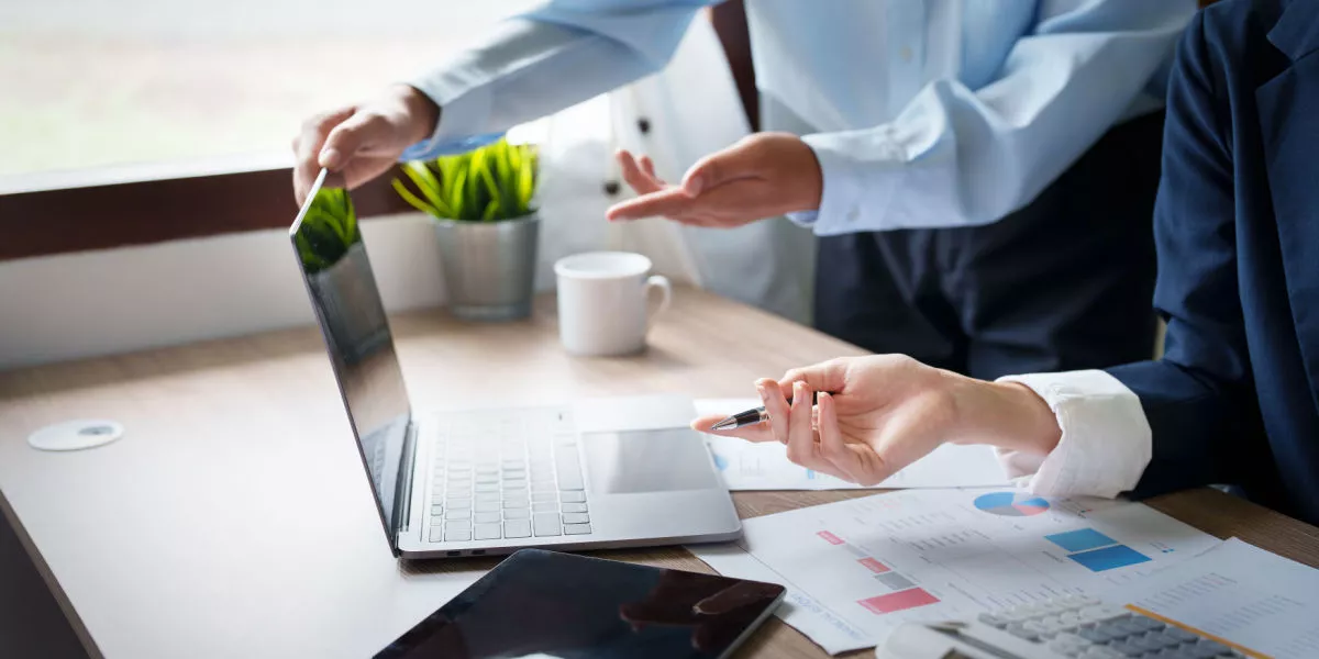 Office workers pointing to a laptop with graphs on the desk.