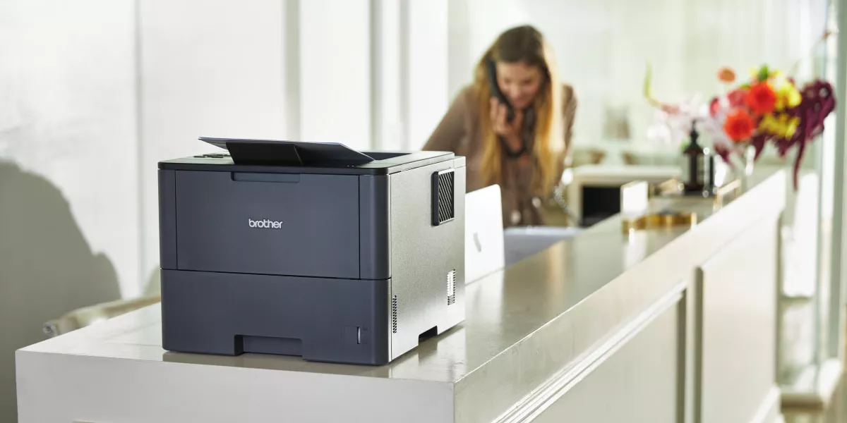 A Brother monochrome printer with a small business owner writing a tech grant proposal in the background