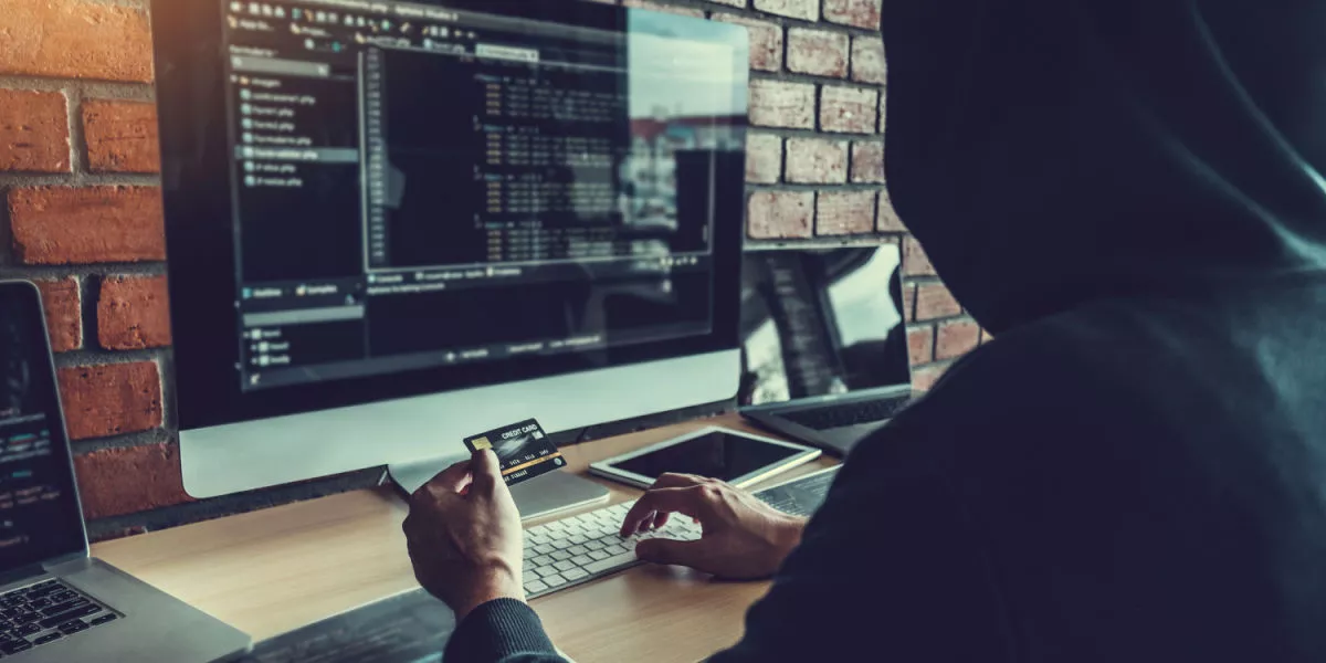 A hacker with a credit card in front of a computer with a dark screen.