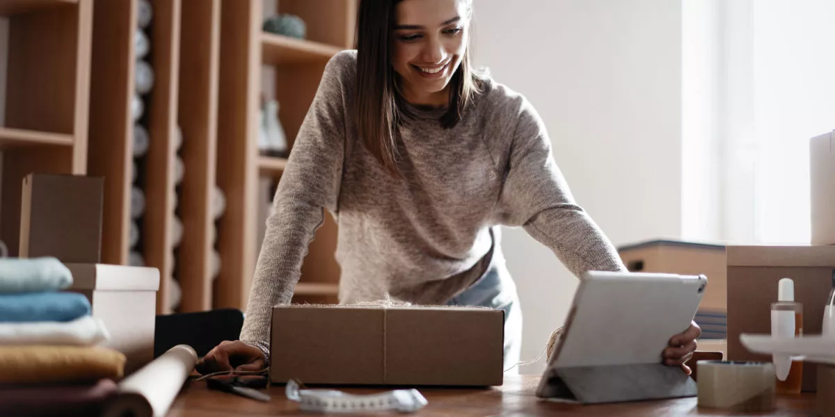 A female ecommerce business owner in a workshop on a laptop with stock in background. 