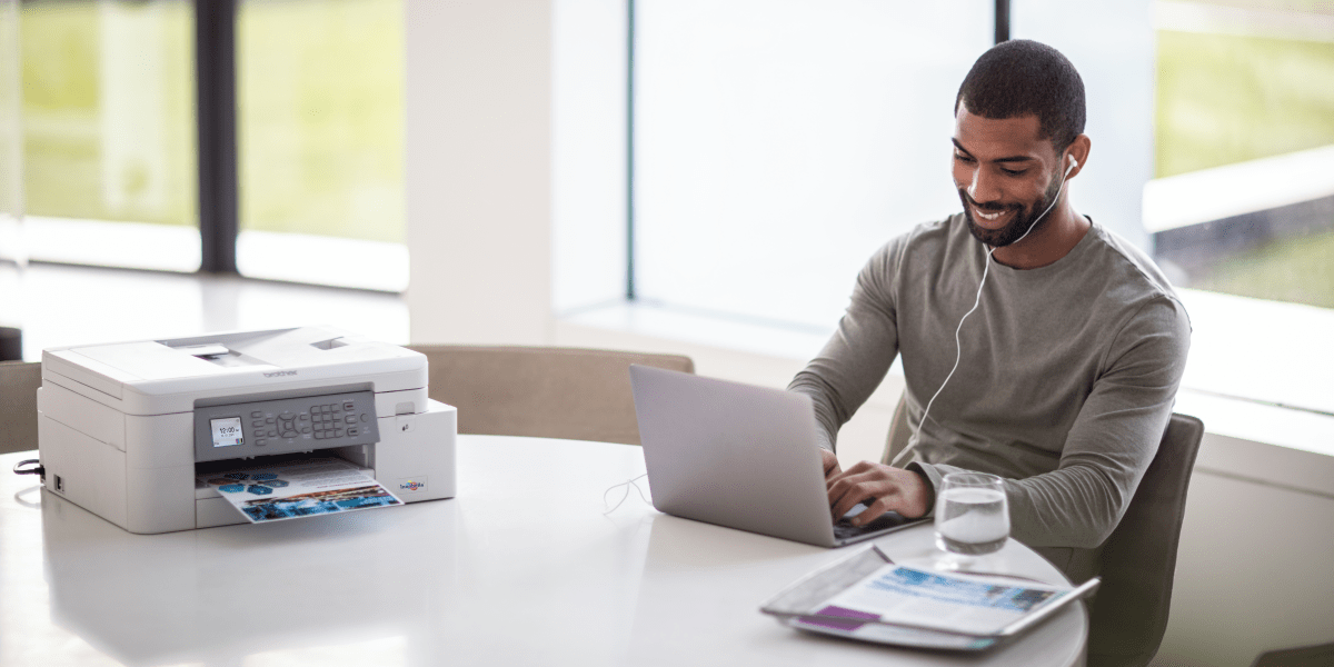 A male freelance worker next to a laptop and a Brother inkjet printer