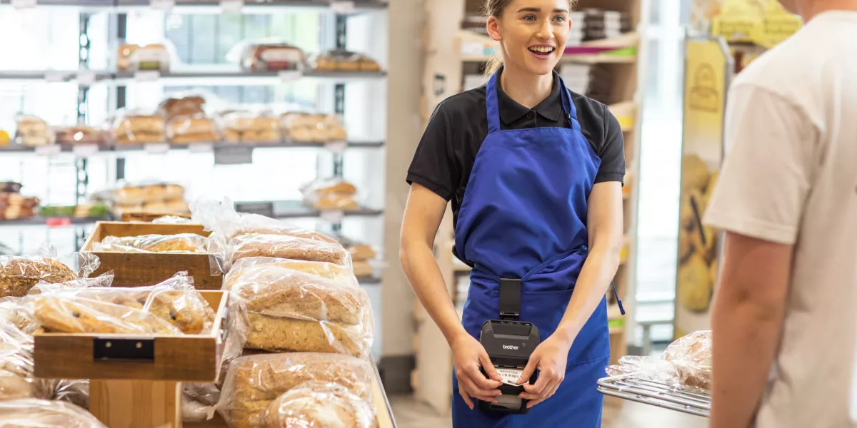 A retail worker with a portable printer strapped to her shoulder printing shelf labels