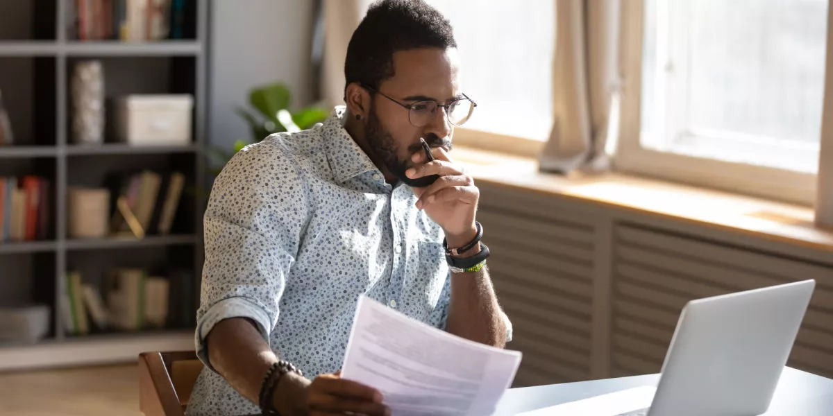 A male freelancer with documents in hand looking at a laptop