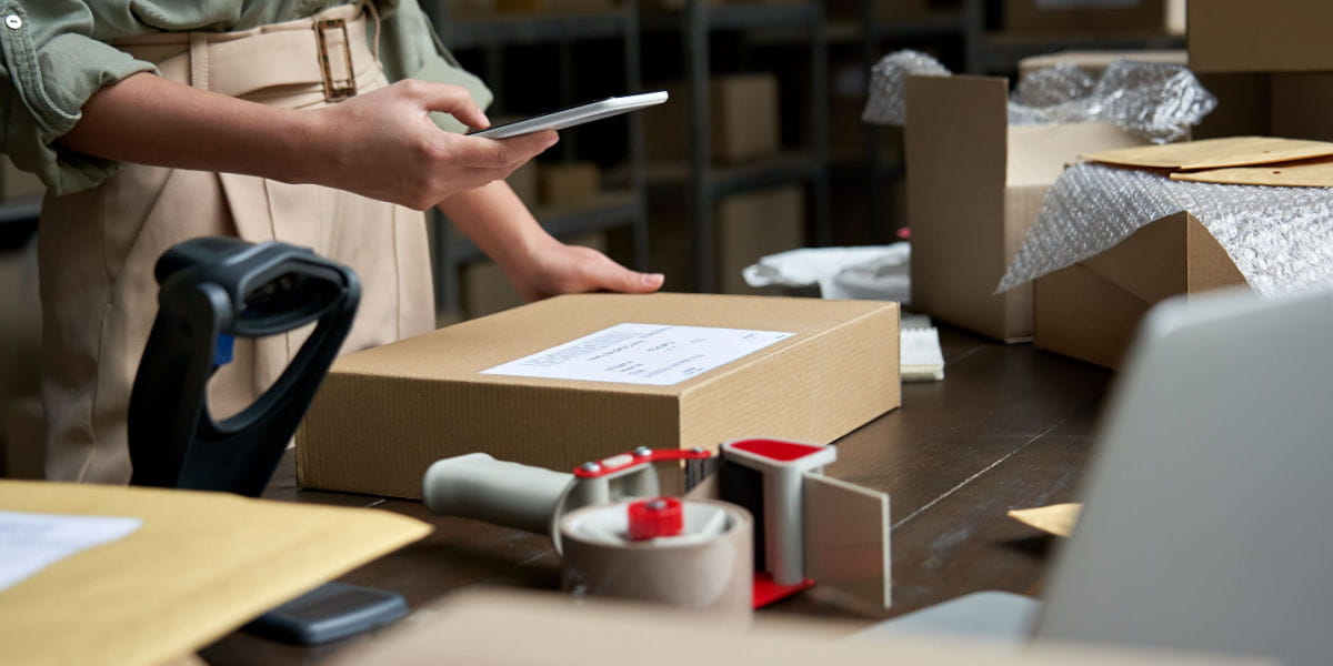 A business owner scanning a parcel with a smartphone in a warehouse.