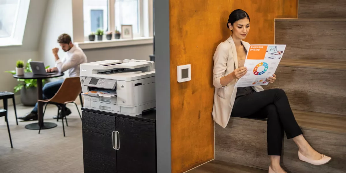 Two workers with one holding a printed brand design next to a business inkjet printer