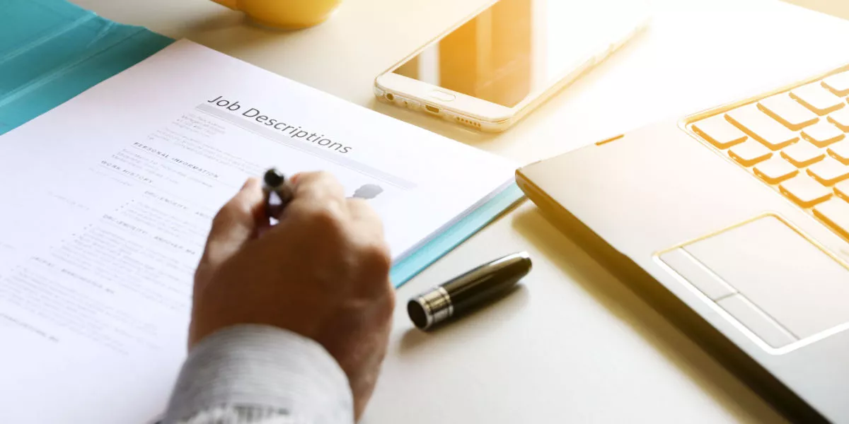 Man's hand next to a job description and laptop